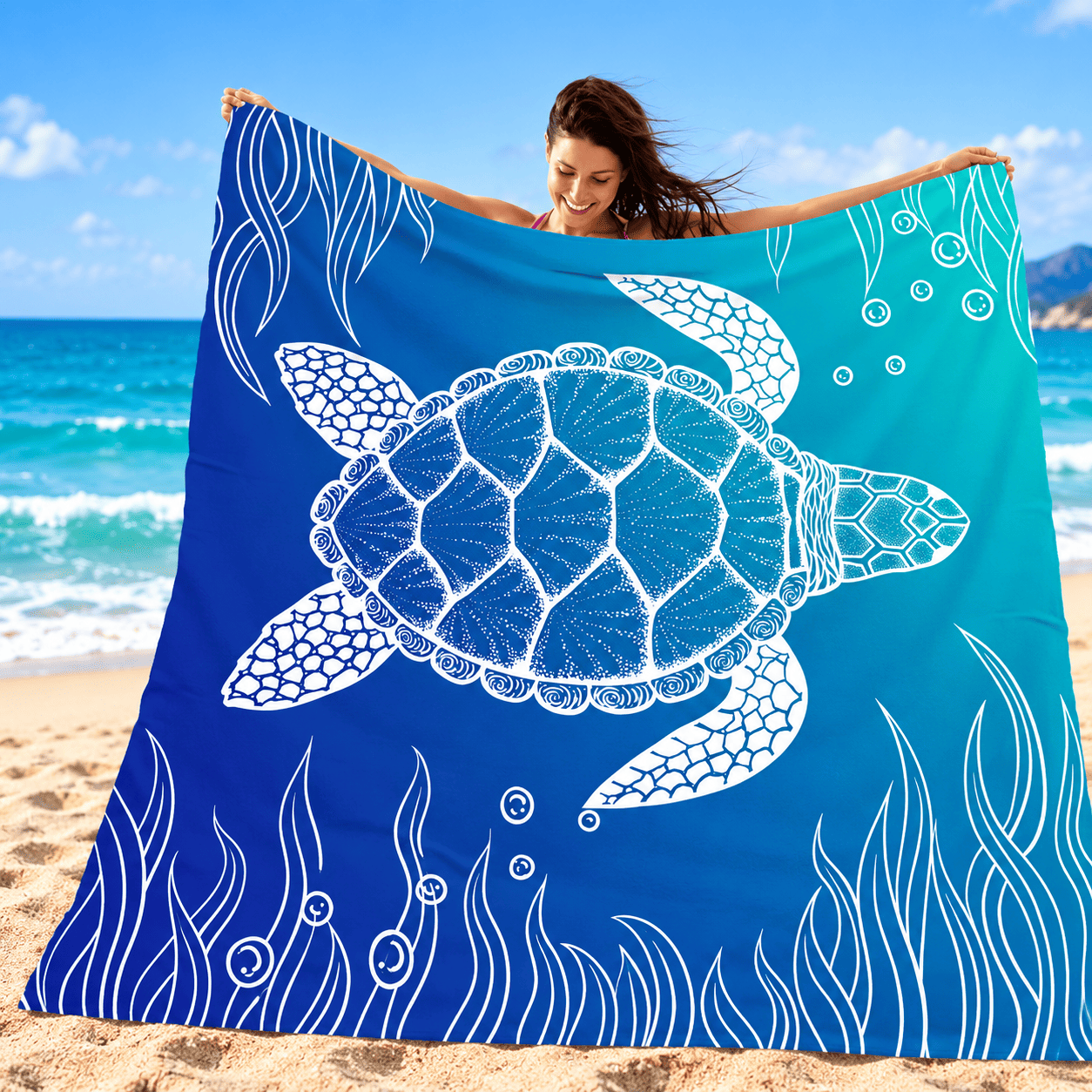 Portable Beach Mat – Sandproof Waterproof Camping & Picnic Blanket A woman on a sandy beach holds up a large square blue towel or blanket featuring a white sea turtle and underwater wave design. The background shows the ocean, sky, and beach.