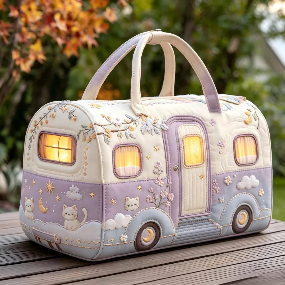Christmas Quilted Travel Tote Bag – Vintage Camping Car Handbag A whimsical quilted handbag shaped like a vintage camper trailer, featuring embroidered cats, stars, clouds, and flowers, with warm glowing window lights, set on a wooden deck with a blurred garden background.