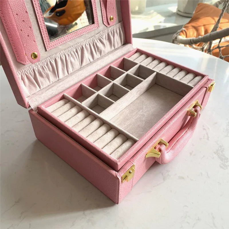 Leather Travel Jewelry Box with Mirror – Double-Layer Jewelry Organizer A pink textured leather jewelry organizer case with an open lid, featuring multiple compartments, ring rolls, a mirror, and gold-tone hardware, set on a white marble tabletop.