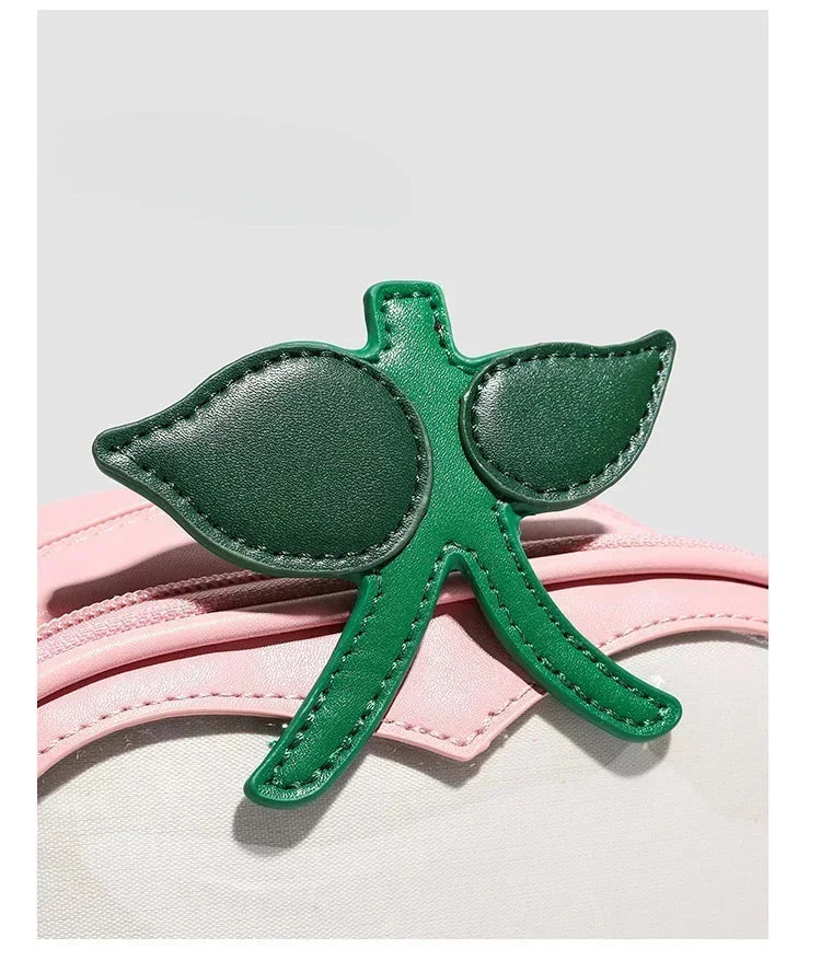 Apple-Shaped Crossbody Phone Purse – Lightweight Shoulder Bag A green leather accessory shaped like a stylized leaf or clover, placed on top of a light pink strap against a light gray background.