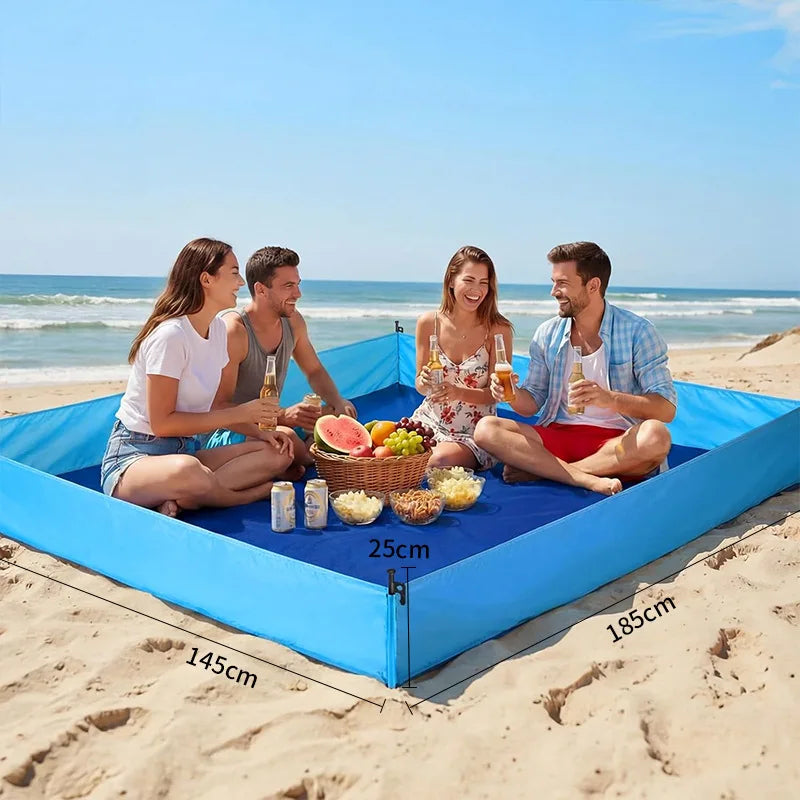 Foldable Portable Beach Mat – Waterproof Camping & Picnic Blanket A blue inflatable beach blanket with a built-in umbrella frame is set up on a sandy beach with four people sitting inside, holding drinks and enjoying a picnic. The image includes dimension labels showing the blanket's size (145cm by 185cm by 25cm).