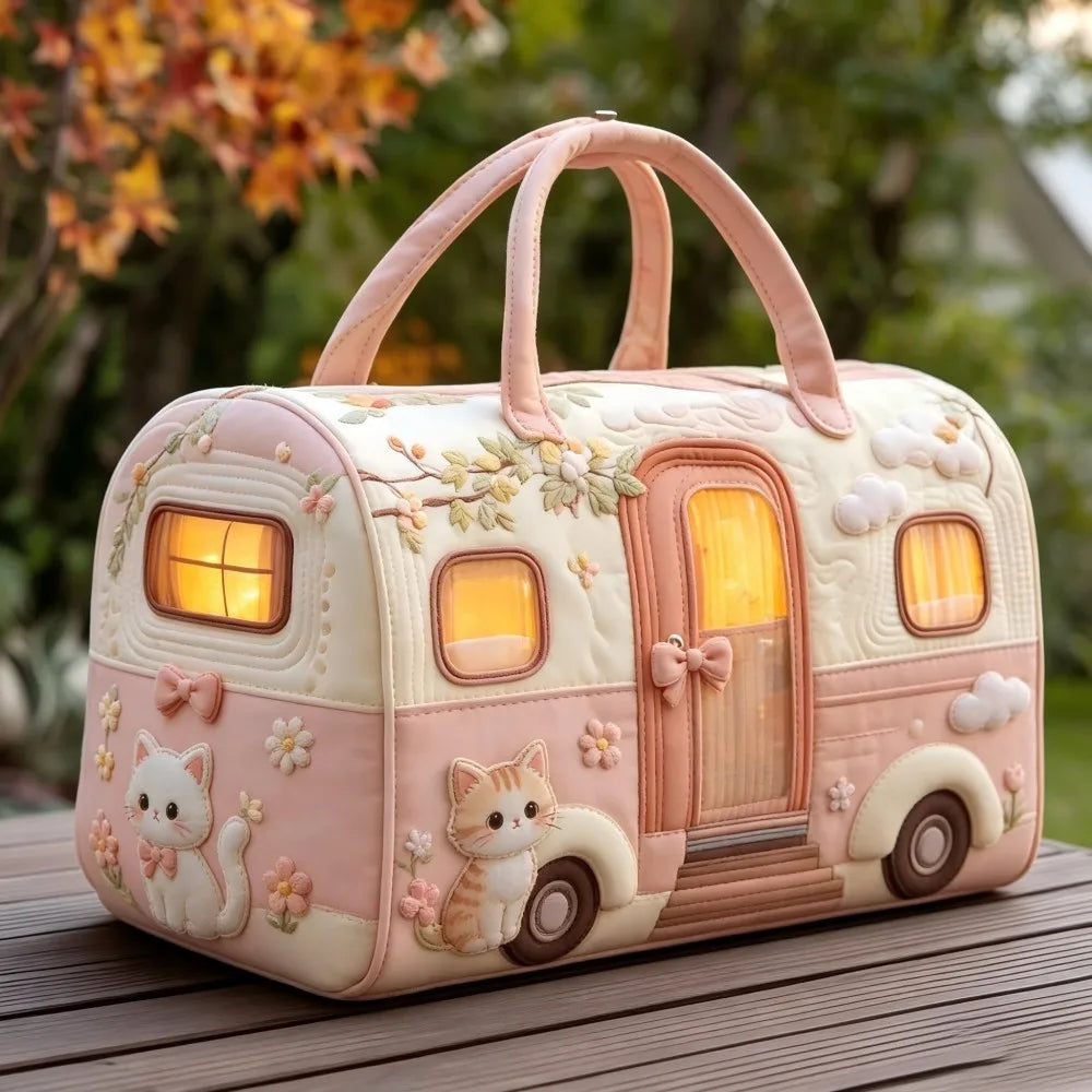 Christmas Quilted Travel Tote Bag – Vintage Camping Car Handbag A decorative pink and cream travel trailer-shaped handbag with cat and floral details, photographed outdoors on a wooden surface with blurred foliage in the background.