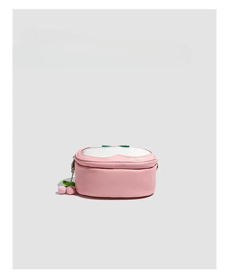 Apple-Shaped Crossbody Phone Purse – Lightweight Shoulder Bag A pink oval-shaped shoulder bag with a white top flap featuring a pink heart design, a small green bow, and a dangling pink rose charm, shown on a light gray background.