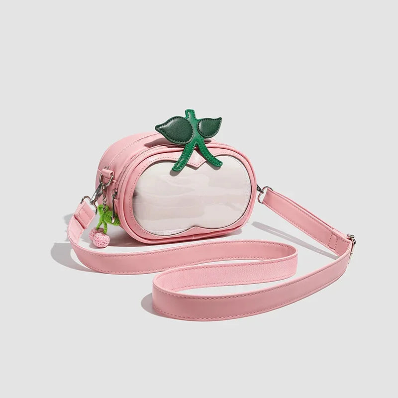 Apple-Shaped Crossbody Phone Purse – Lightweight Shoulder Bag A pink faux-leather crossbody bag shaped like a peach, featuring a clear front window, a green leaf accent on top, and a long matching pink strap, shown on a light gray background.