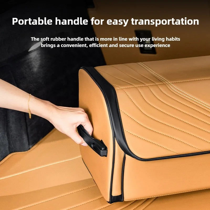 Luxury Leather Car Trunk Organizer – Large Foldable Storage Box A tan faux-leather storage cube with a black handle and trim, shown with a hand holding the handle. White text at the top reads 'Portable handle for easy transportation' and describes the soft rubber handle.