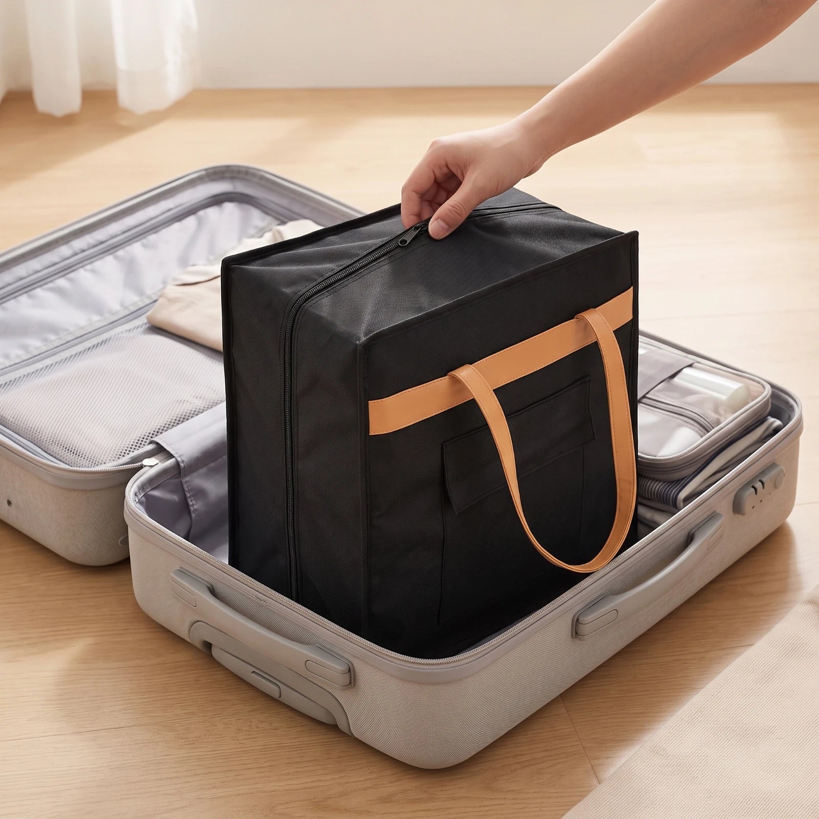 6-Pair Travel Shoe Bag – Large Capacity Oxford Cloth Organizer A black fabric travel organizer bag with tan handles is being placed into an open light gray suitcase on a wooden floor. A person's hand is visible holding the top of the bag.
