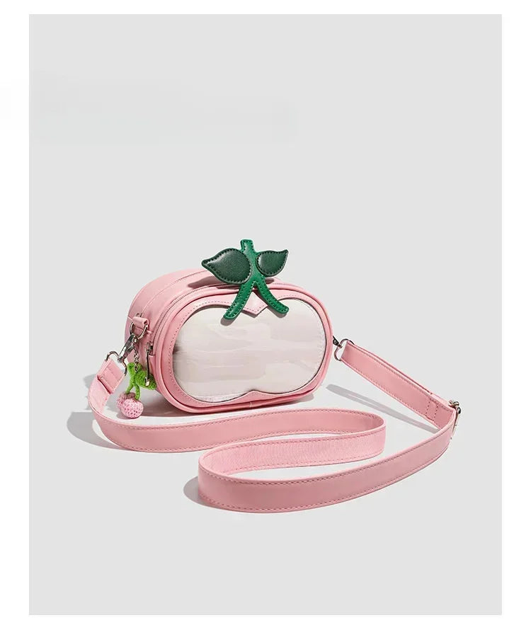 Apple-Shaped Crossbody Phone Purse – Lightweight Shoulder Bag A pink faux-leather crossbody bag designed to look like a peach, featuring a clear front panel, a green leaf and stem accent on top, and a matching pink shoulder strap, shown against a light gray background.