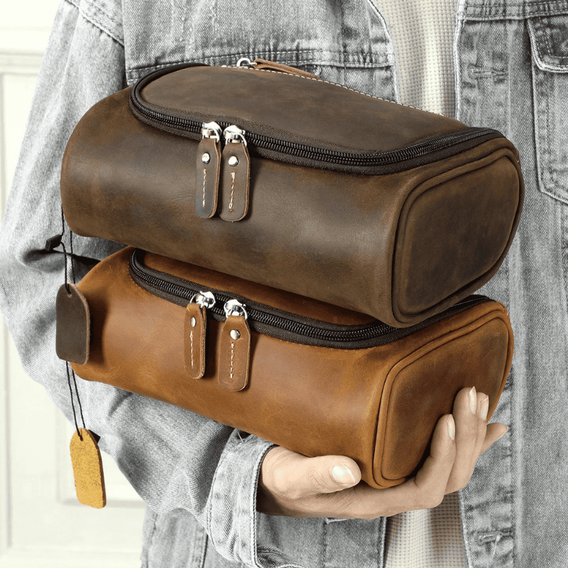 Top-Grain Leather Toiletry Bag for Men – Vintage Travel Organizer Pouch Two cylindrical leather zippered cases in dark brown and medium brown are stacked and held by a person wearing a light gray denim jacket.