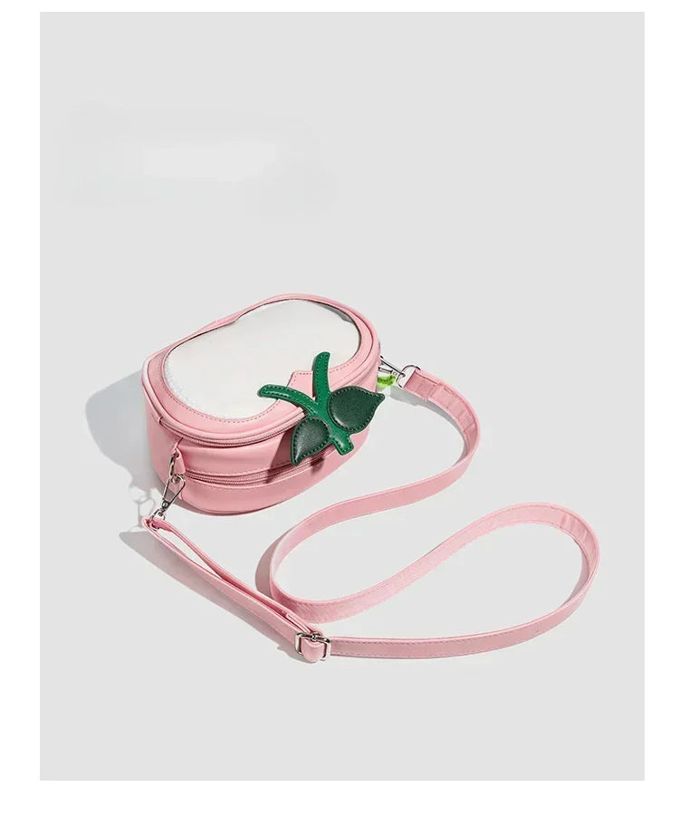 Apple-Shaped Crossbody Phone Purse – Lightweight Shoulder Bag A pink faux-leather crossbody bag with a white oval front pocket, a green felt pineapple accent on the front, and a matching pink shoulder strap, shown on a light gray background.