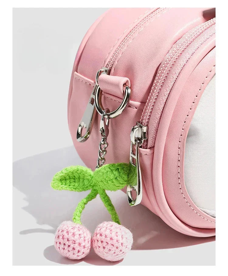 Apple-Shaped Crossbody Phone Purse – Lightweight Shoulder Bag A pink nylon shoulder bag with a decorative cherry keychain charm featuring green leaves and two pink-and-white crocheted cherries, shown on a light gray background.