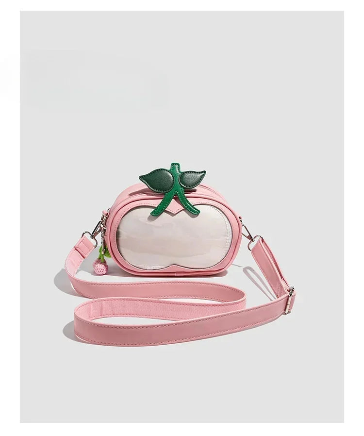 Apple-Shaped Crossbody Phone Purse – Lightweight Shoulder Bag A pink faux-leather crossbody bag designed to look like a peach, featuring a clear front panel, a green leaf and stem accent on top, and a long matching pink strap, shown against a light gray background.