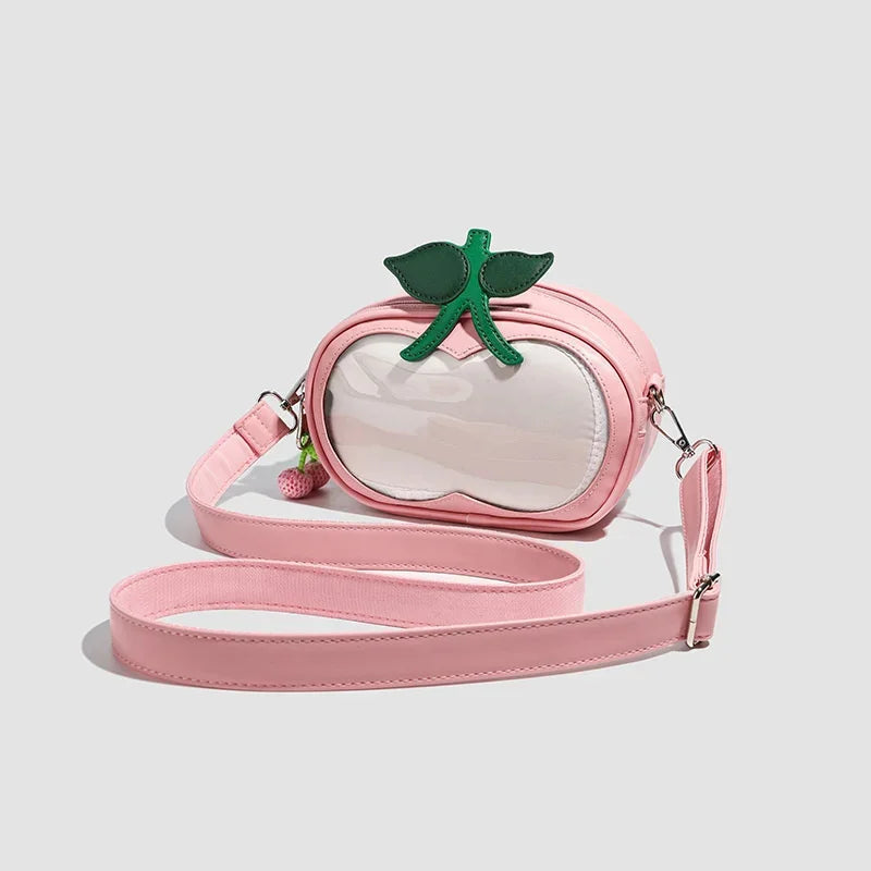 Apple-Shaped Crossbody Phone Purse – Lightweight Shoulder Bag A pink faux-leather crossbody bag designed to look like a peach, featuring a clear front window, a green leaf and stem detail on top, and a long matching pink strap, shown on a light gray background.
