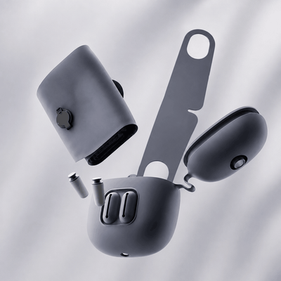 A matte dark gray wireless earbud charging case shown disassembled with its lid, charging contacts, and a long metal accessory piece floating against a soft light gray background.