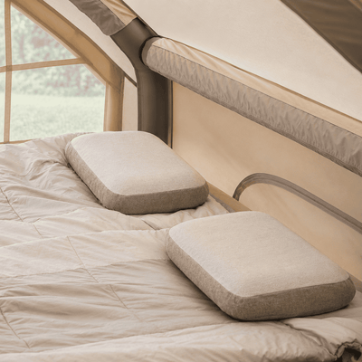 Two rectangular camping pillows with a light beige textured fabric and gray-green edges, resting on a beige quilted sleeping pad inside a tent.