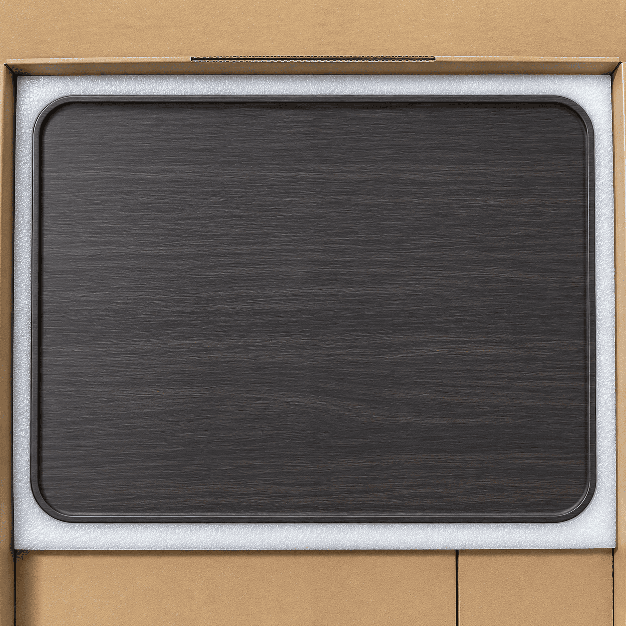 A dark charcoal gray wood-grain rectangular tray or mat with rounded corners, shown resting on a white foam insert inside a brown cardboard box.