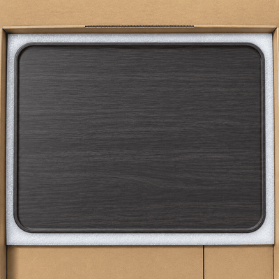 A dark charcoal gray wood-grain rectangular tray or mat with rounded corners, shown resting on a white foam insert inside a brown cardboard box.