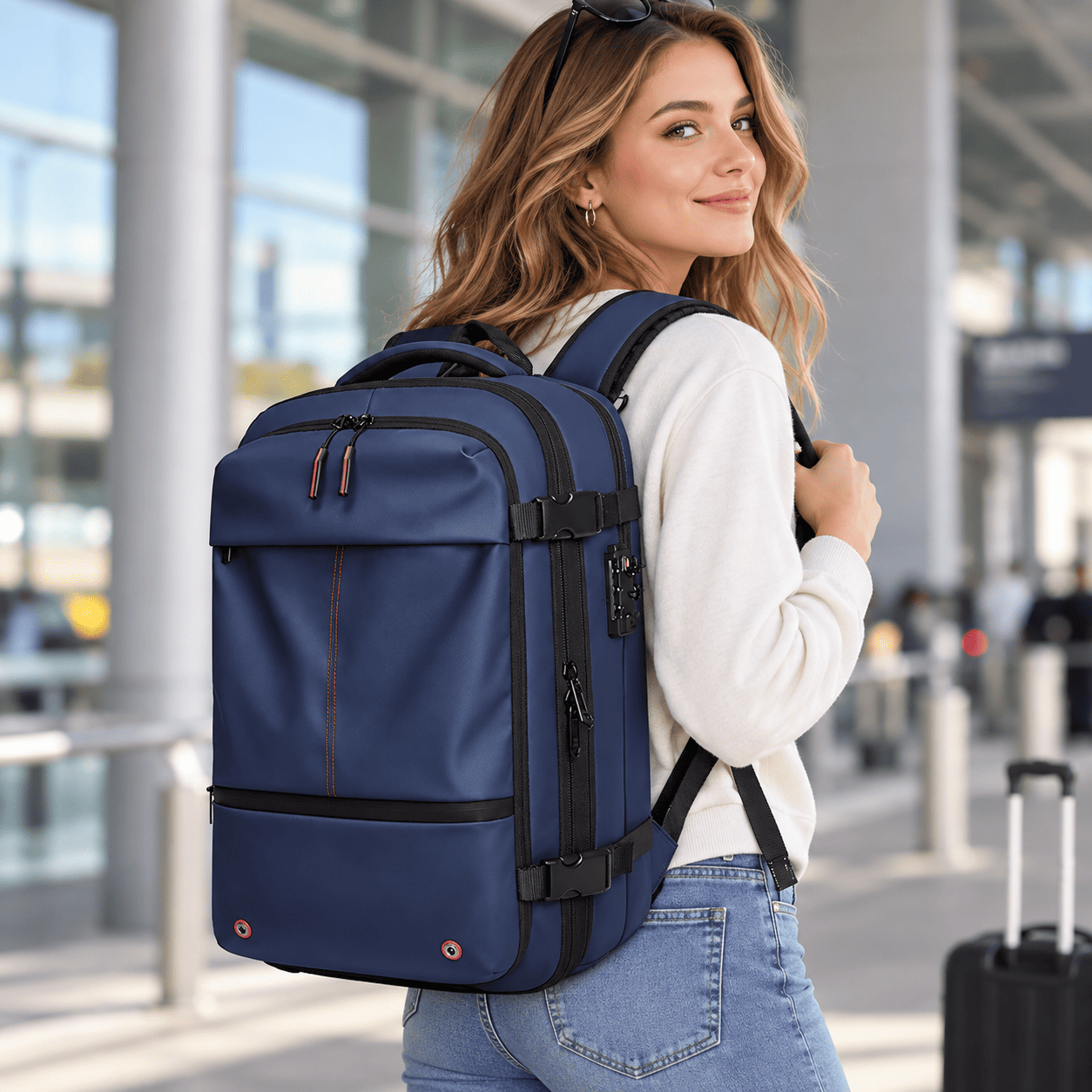 A woman wearing a navy blue and black travel backpack with multiple compartments, shown in a modern airport or transit station setting.