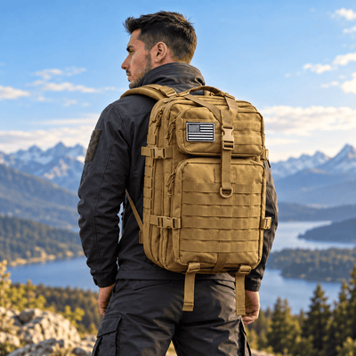 A man wearing a tan tactical backpack with a US flag patch, photographed from behind against a scenic mountain and lake background.