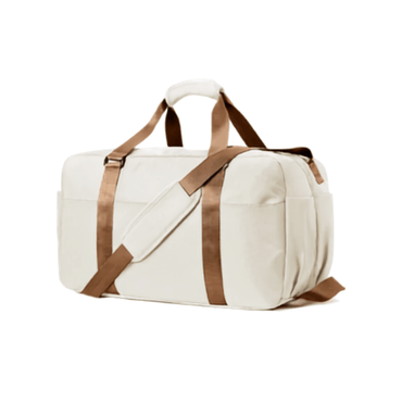 An off-white canvas duffel bag with brown straps and trim, shown from a three-quarter angle on a solid white background.
