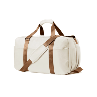An off-white canvas duffel bag with brown straps and trim, shown from a three-quarter angle on a solid white background.