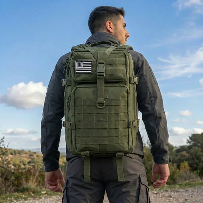 A man wearing an olive green tactical backpack with a US flag patch on the front, photographed from behind against an outdoor sky background.