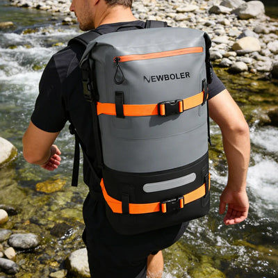 Person wearing a gray and orange backpack with 'NEWBOLER' branding by a stream.
