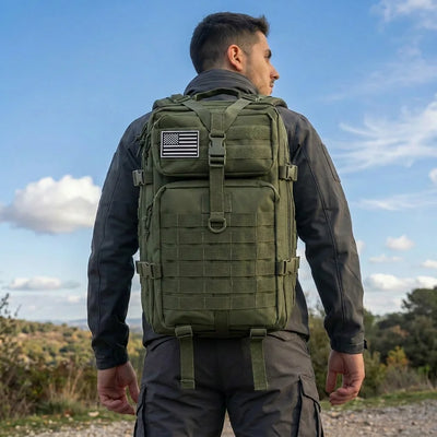 A man wearing an olive green tactical backpack with a US flag patch on the front, photographed from behind against an outdoor sky background.