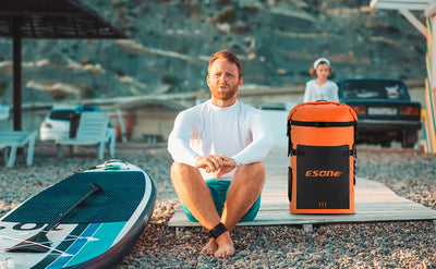 Man sitting on a beach with a paddleboard and Esone bag