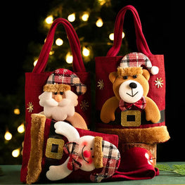 Decorative gift bags with Santa Claus, reindeer, and bear figures against a blurred Christmas tree background.