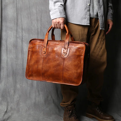 Person holding a brown leather briefcase against a gray background
