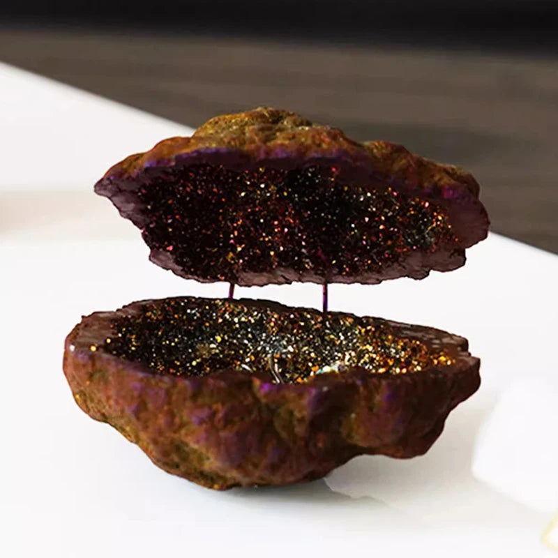 A shell-shaped jewelry box made from a natural iridescent mineral or geode, shown open on a white background. The exterior has a textured, metallic copper-brown and purple surface, while the interior is lined with dark glitter and holds a small clear faceted crystal earring.