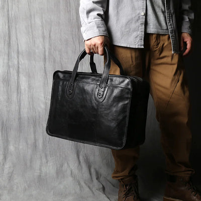 Person holding a black leather briefcase against a gray background