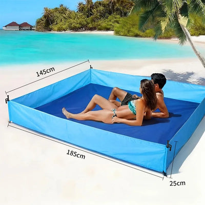A large square inflatable beach pool or lounge mat in blue is set on a sandy tropical beach with a couple reclining inside. White dimension lines and text show measurements of 145 cm width, 185 cm length, and 25 cm depth.