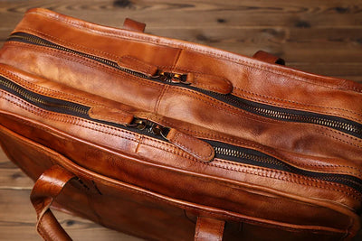 Brown leather bag with zippers on a wooden surface