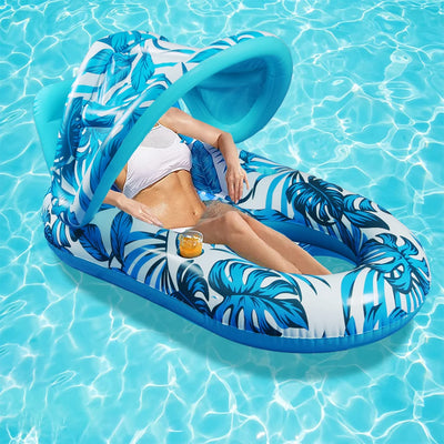 A woman reclines on a tropical leaf-patterned inflatable pool float with a built-in sun canopy in a bright swimming pool.