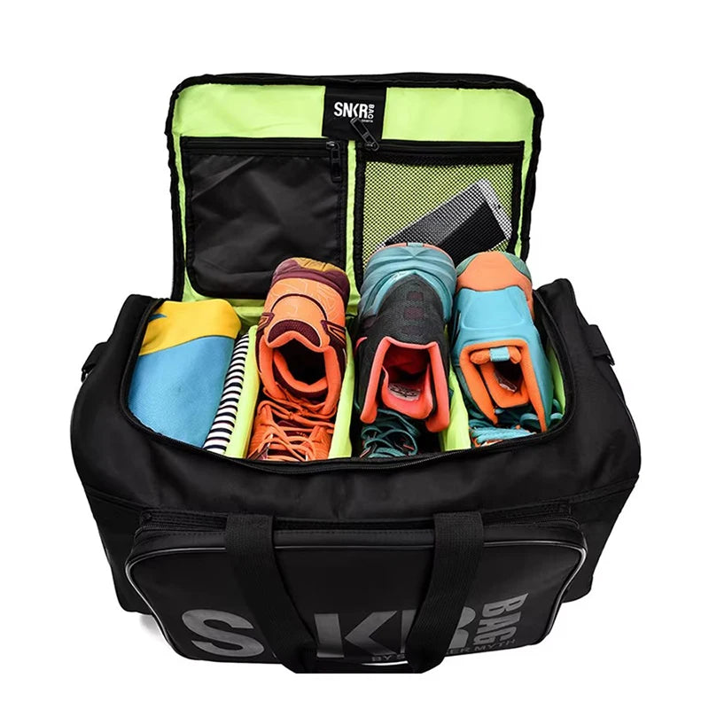 A black duffel bag with a bright neon green interior, shown open to reveal multiple compartments, mesh pockets, and side handles. The bag has large white stylized lettering on the front pocket and is photographed on a clean light gray studio background.