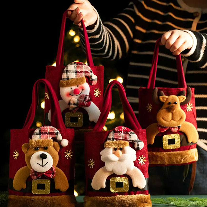 Four red Christmas-themed fabric tote bags with plush animal faces and holiday decorations, held by a person wearing a striped sweater against a dark background with warm blurred lights.