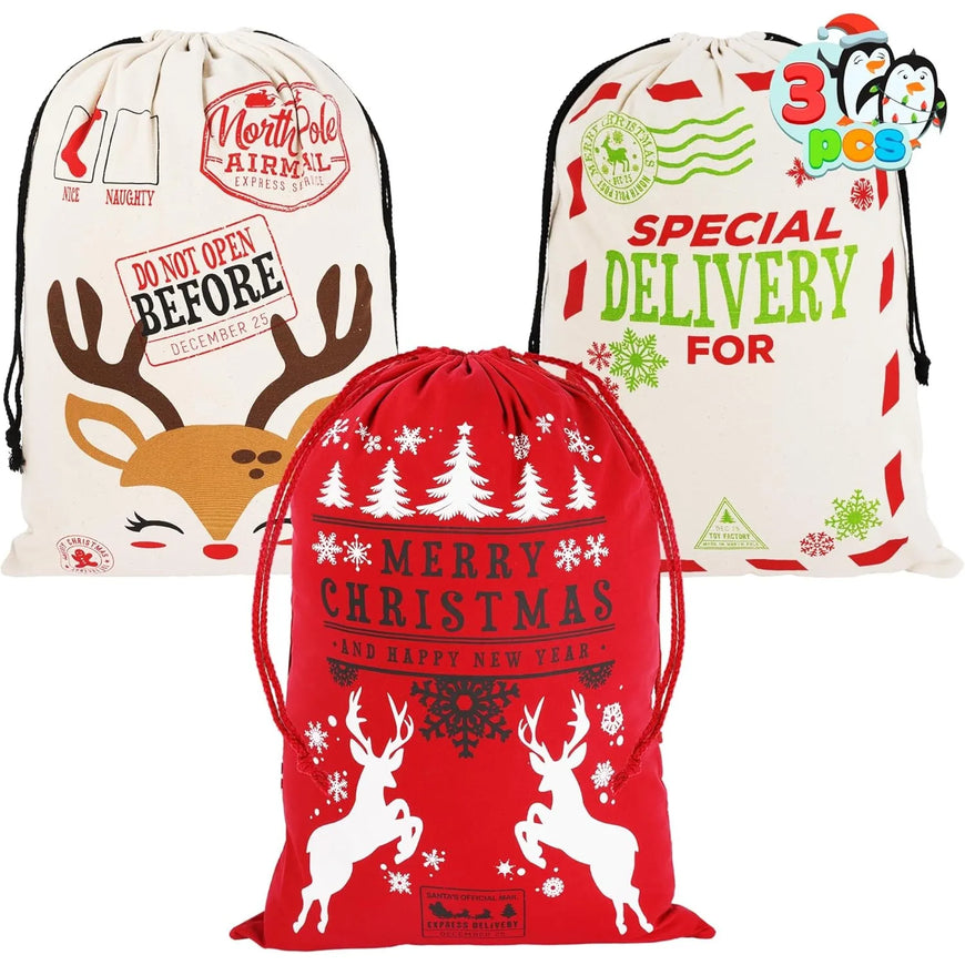 Three Christmas-themed drawstring Santa bags shown on a plain white background: one cream bag with reindeer antlers and holiday text, one cream bag with green and red delivery text, and one red bag with white reindeer silhouettes and snowflakes.
