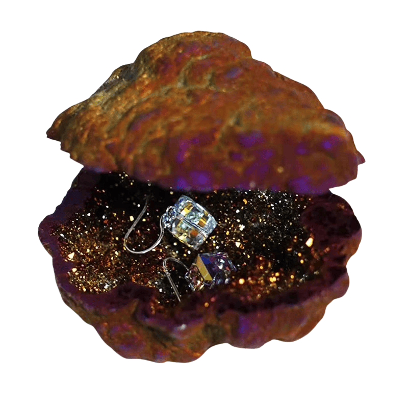 A shell-shaped jewelry box made from a natural iridescent mineral or geode, shown open on a white background. The exterior has a textured, metallic copper-brown and purple surface, while the interior is lined with dark glitter and holds a small clear faceted crystal earring.