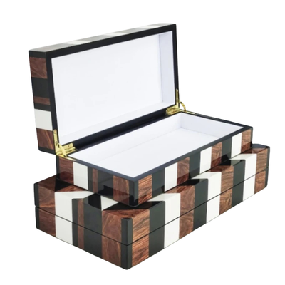 A rectangular open jewelry box with a striped pattern of dark brown wood grain, black, and white inlays, featuring gold-tone metal hinges and a white interior lining.