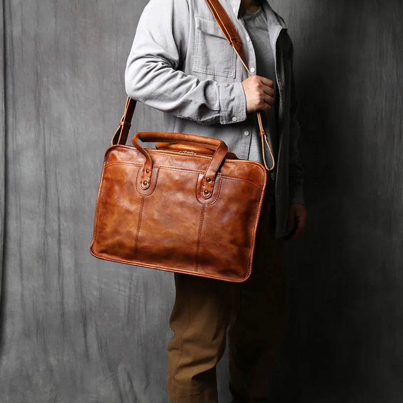 A brown leather briefcase with dual top handles, a front zippered pocket, and a main zippered compartment, shown on a clean white background.