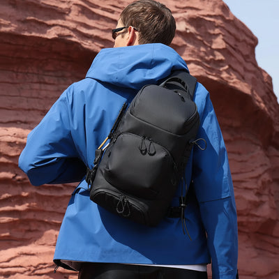 A man wearing a blue hooded jacket and sunglasses, shown from behind with a black BANGE backpack on his back, set against a red rock desert background.