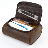 A brown faux-leather toiletry bag shown open, revealing its interior compartments, mesh pockets, and storage space filled with travel items, on a white background.