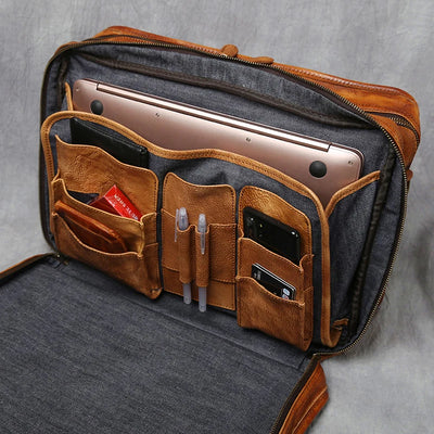 An open brown leather laptop bag with a gray fabric interior, shown holding a laptop, phone, pens, and cards in its organized pockets.