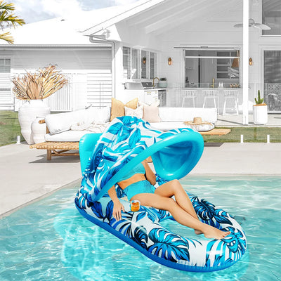 Person lounging on a blue and white patterned inflatable pool float in a pool area with a house in the background.